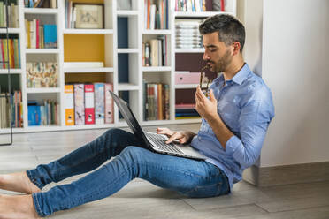 Junger Mann sitzt zu Hause auf dem Boden und benutzt einen Laptop - MGIF00856