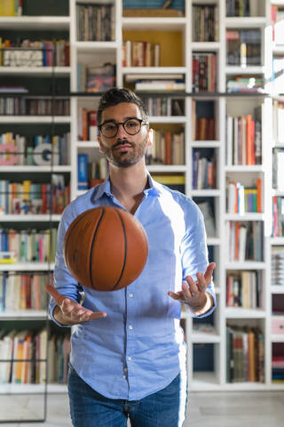 Porträt eines jungen Mannes mit Basketball, der zu Hause vor einem Bücherregal steht, lizenzfreies Stockfoto