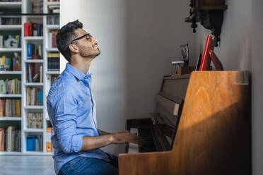 Lächelnder junger Mann mit geschlossenen Augen, der zu Hause Klavier spielt - MGIF00881