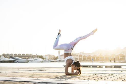 Asiatische Frau übt Yoga auf einem Pier am Hafen - RCPF00101