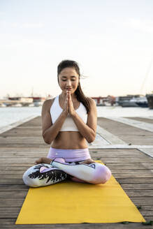 Asiatische Frau, die auf einem Pier am Hafen Yoga praktiziert und meditiert - RCPF00121