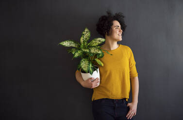 Portrait of young woman holding a house plant and looking sideways - HAPF03090