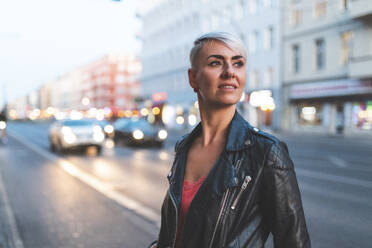 Porträt einer blonden Frau, die abends am Straßenrand steht, Berlin, Deutschland - WPEF02250