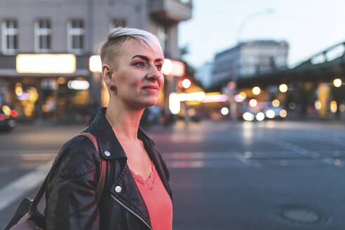 Porträt einer lächelnden blonden Frau am Straßenrand am Abend, Berlin, Deutschland - WPEF02251