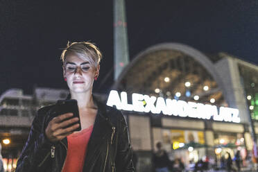 Porträt einer blonden Frau, die am Alexanderplatz steht und ein Mobiltelefon benutzt, Berlin, Deutschland - WPEF02260