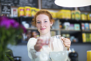 Junge Frau, die in einem Café arbeitet und ein Wasserglas reicht - SGF02433