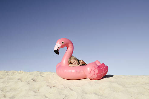 Lächelndes Mädchen, das auf einem Flamingo-Schwimmkörper liegt und in die Kamera schaut - EYAF00638