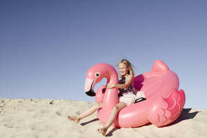 Lächelndes kleines Mädchen mit Flamingo-Poolschwimmer auf dem Sand - EYAF00639