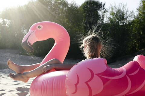 Mädchen sitzt auf Flamingo-Poolschwimmer, lizenzfreies Stockfoto