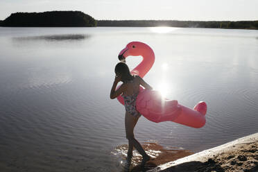 Young man with flamingo pool float in the lake - EYAF00643