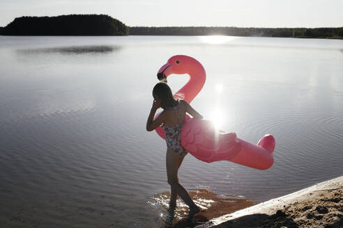 Junger Mann mit Flamingo-Schwimmer im See - EYAF00643