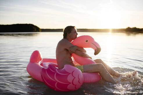 Young man with flamingo pool float on a lake - EYAF00649