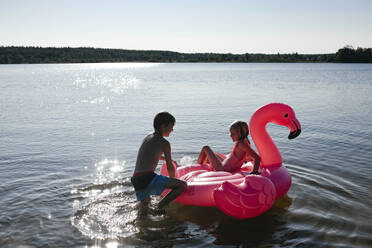 Bruder und Schwester mit Flamingo-Poolschwimmer auf dem See - EYAF00653