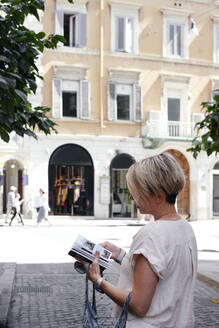 Frau schaut in einen Reiseführer in der Stadt, Rom, Italien - EYAF00663