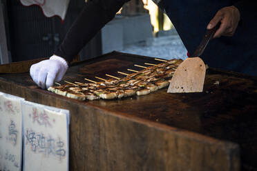 Japan, Kyoto Prefecture, Kyoto City, Hands of chef preparing yakitori at food stand - ABZF02796