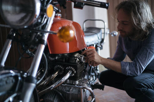 Junger Mann überprüft sein in der Garage geparktes Oldtimer-Motorrad - JPIF00234