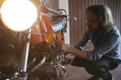 Junger Mann überprüft sein in der Garage geparktes Oldtimer-Motorrad - JPIF00235