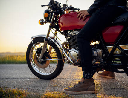 Ausschnittaufnahme eines Mannes auf seinem Motorrad bei Sonnenuntergang, Toskana, Italien - JPIF00241