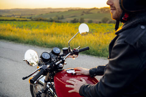 Ausschnittaufnahme eines Mannes auf seinem Oldtimer-Motorrad bei Sonnenuntergang, Toskana, Italien, lizenzfreies Stockfoto