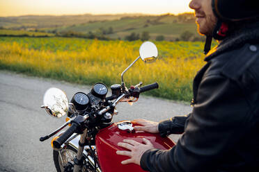 Ausschnittaufnahme eines Mannes auf seinem Oldtimer-Motorrad bei Sonnenuntergang, Toskana, Italien - JPIF00242