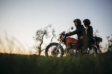 Junges Paar auf Oldtimer-Motorrad in ländlicher Szene bei Sonnenuntergang - JPIF00246