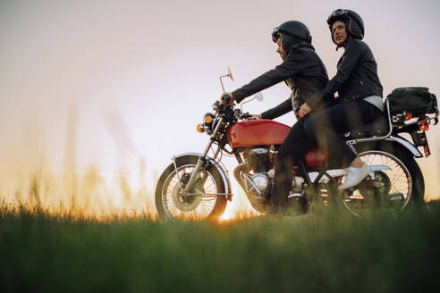 Junges Paar auf Oldtimer-Motorrad bei Sonnenuntergang - JPIF00247