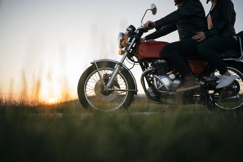 Ausschnittaufnahme eines Paares auf einem Oldtimer-Motorrad bei Sonnenuntergang - JPIF00248