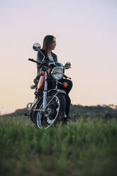 Junge Frau mit Oldtimer-Motorrad in ländlicher Umgebung genießt den Sonnenuntergang - JPIF00257