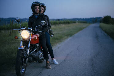 Porträt eines jungen Paares auf einem Oldtimer-Motorrad am Straßenrand - JPIF00259