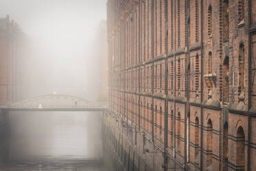 Germany, Hamburg, Speicherstadt, Building and footbridge over canal in fog - KEBF01417