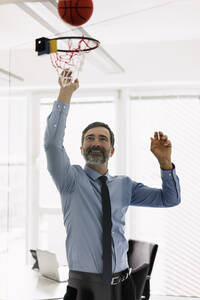 Glücklicher reifer Geschäftsmann spielt Basketball im Büro - MOEF02514