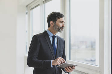 Älterer Geschäftsmann mit Tablet im Büro und Blick aus dem Fenster - MOEF02519