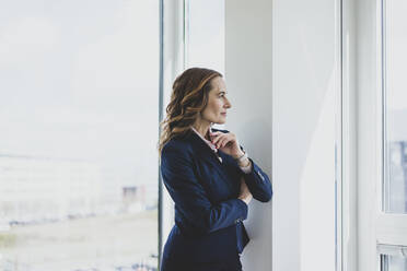 Mature businesswoman looking out of window in office - MOEF02521