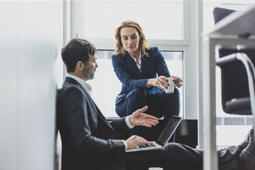 Businesswoman with businessman in office sitting on the floor using laptop - MOEF02528