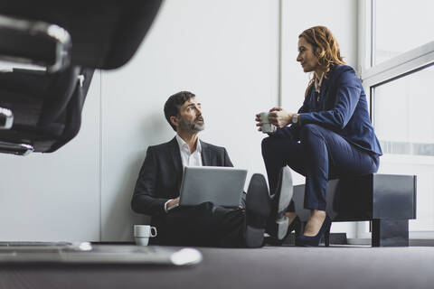 Geschäftsfrau mit Geschäftsmann im Büro auf dem Boden sitzend mit Laptop, lizenzfreies Stockfoto