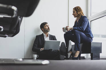 Businesswoman with businessman in office sitting on the floor using laptop - MOEF02534