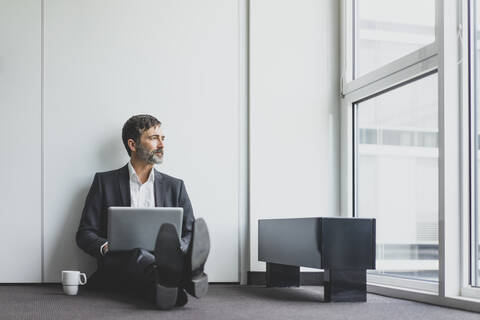 Mature businessman in office sitting on the floor with laptop stock photo