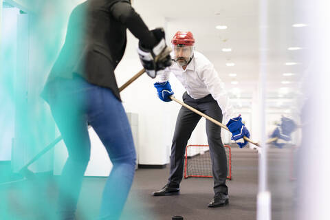 Geschäftsfrau und Geschäftsmann spielen Eishockey im Büro, lizenzfreies Stockfoto