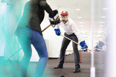 Businesswoman and businessman playing ice hockey in office - MOEF02545