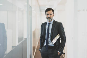 Portrait of serious mature businessman standing on office corridor - MOEF02549