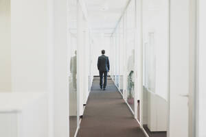 Rückansicht eines Geschäftsmannes, der einen Bürokorridor entlang geht - MOEF02560