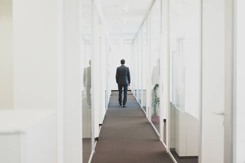 Rear view of businessman walking down office corridor - MOEF02560