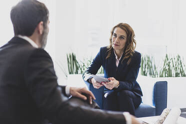 Businesswoman and businessman sitting in armchairs in office talking - MOEF02566