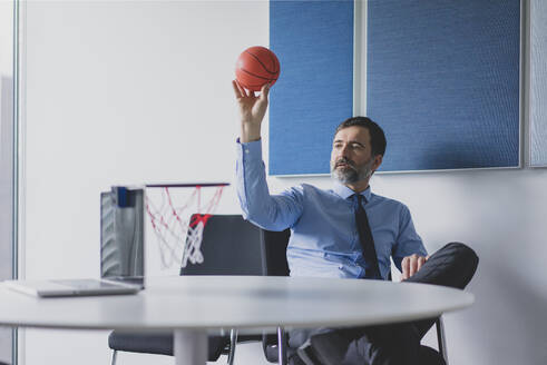 Älterer Geschäftsmann spielt Basketball im Büro - MOEF02568