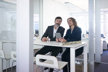 Geschäftsfrau und Geschäftsmann mit Tablet sitzen am Schreibtisch im Büro - MOEF02571
