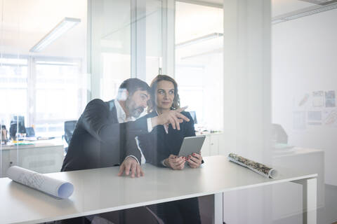 Geschäftsfrau und Geschäftsmann mit Tablet sitzen am Schreibtisch im Büro, lizenzfreies Stockfoto
