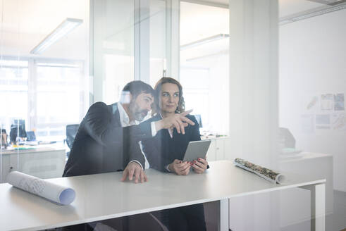 Businesswoman and businessman with tablet sitting at desk in office - MOEF02572