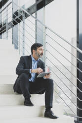 Mature businessman sitting on stairs with tablet - MOEF02580