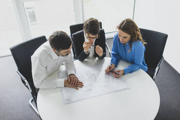 Geschäftsmann und zwei Geschäftsfrauen arbeiten an einem Plan auf dem Schreibtisch im Büro - MOEF02594