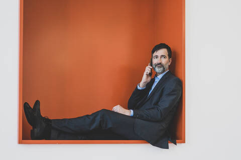 Reifer Geschäftsmann sitzt in einer Nische und spricht mit seinem Handy, lizenzfreies Stockfoto